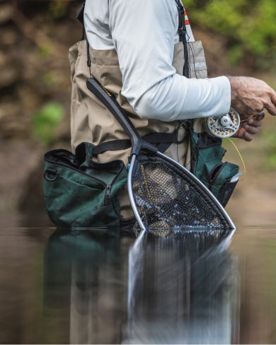 Guy in wading gear with a fishing net waist deep in water